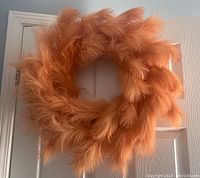 Front view of a pampas grass wreath with soft fluffy orange-beige plumes, hanging on a white door, showing full circular shape.