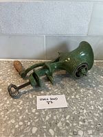 Side view of vintage green enamel meat grinder showing clamp and wooden handle.