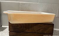 Photo showing the full side view of the vintage peach lustre rectangular casserole dish with handle on one side.