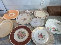 Group of nine vintage decorative plates on countertop showing various floral designs and border styles