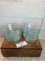 Nine vintage Pyrex glass bowls stacked in two groups on wood block with small note showing max bid and set price.