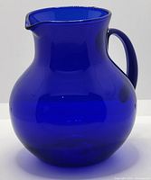 Front view of cobalt blue glass pitcher showing bulbous rounded body and pouring spout.