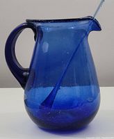 Side angle view of the cobalt blue glass pitcher with visible stir stick inside, highlighting handle and pouring spout.