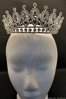 Front view of the sparkling tiara on a mannequin head showing the teardrop and round rhinestones and the overall shape and design.