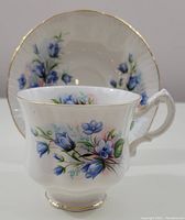 Side view of the Paragon cup showing blue floral design and white porcelain with gold rim and base, with matching saucer in background