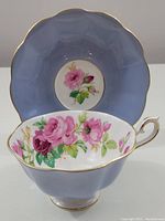 Wide mouth tea cup positioned in front of matching saucer showing periwinkle exterior and rose design inside cup and center of saucer