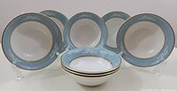 Eight Simpson Potters Skye pattern cereal/soup bowls arranged in a standing and stacked display, showing the blue rim with white floral design and gold trim.