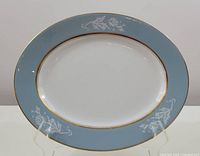 Full view showing the oval serving platter with white center, blue rim with white floral motifs, and gold edging.