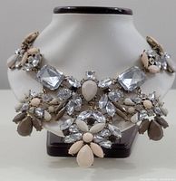 Front view of vintage costume jewelry statement necklace on display stand showing clear and beige rhinestones arranged in a bold design.
