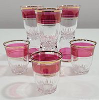 Front view of nine vintage cranberry flash shot glasses showing gold rim and textured bases.