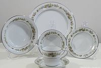 Full set of six pieces shown on display stands: dinner plate, coupe soup bowl, side plate, nappie, tea cup, saucer with floral and fruit motif, silver rims
