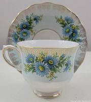Side view of the cup with saucer in background showing floral and gold details on cup and saucer.