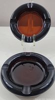 Two vintage brown glass ashtrays, shown from above, highlighting thickness and circular grooves for holding cigarettes.