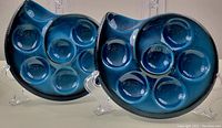 Pair of two teal blue ceramic escargot dishes on clear stands, showing front and top view of both dishes with visible six indentations for escargot.
