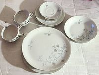 Full set layout showing multiple pieces including dinner plates, smaller plates, bowls, and mugs with floral pattern and subtle blue accents.