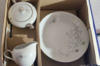 Photo showing sugar bowl with lid, creamer, and dinner plate with floral design on white fine china.