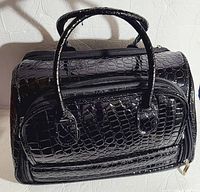 Exterior view showing the black glossy faux alligator texture with handle and zippered compartments.