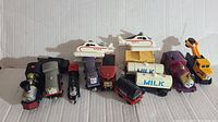 Overview of all toy trains and vehicles arranged side by side on white surface.