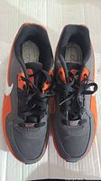 Top view of both sneakers showing the black laces, dark gray and orange color scheme, and white Nike swoosh on the sides.