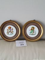 Two framed round miniature pictures hand-painted on porcelain, showing children in vintage style, displayed against a plain wall.