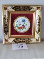 Front view of miniature hand-painted floral porcelain plate in an ornate, gold, black, cream, and red velvet framed artwork.