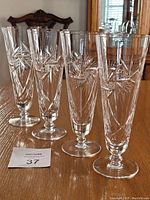 Four tall crystal flute glasses with hand cut starburst patterns, viewed from the front and side on a wooden table.