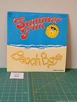Front cover of Beach Boys Summer Fun double vinyl LP album with bright blue sky background, yellow sand script, and smiling sun graphic