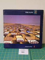 Front cover of Pink Floyd 'A Momentary Lapse of Reason' vinyl album showing multiple beds on a beach with a purple sky and a person making a bed.