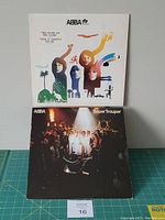Both ABBA vinyl albums front covers displayed together; The Album with colorful abstract artwork, Super Trouper with live band photo.