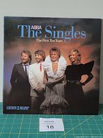 Front cover of ABBA The Singles vinyl LP with band photo and album title.