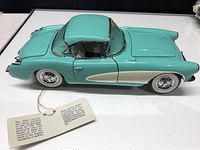 Turquoise 1956 Corvette die cast model car from driver side with attached information tag.
