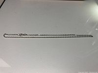 Full length view of the silver necklace laid flat on a white surface, showing the entire chain and clasp.