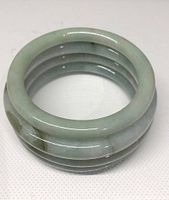 Four stacked jade bangle bracelets in pale green/white color with natural stone patterning.