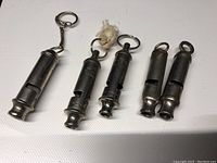 Overview of lot showing all 5 vintage whistles laid out on white surface
