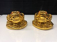 Front view of two gold-tone lucky coin frog figurines with red eyes