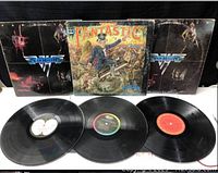 Photo shows three vinyl albums with their covers behind. Two black Van Halen album covers on sides, one colorful Fantastic album cover center. Vinyl records laid out below covers.