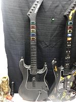 Close up of two black guitar controllers with colored fret buttons, showing details of neck and bodies.