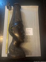 Full side view of dark hardwood African statue with measuring tape showing approximate height of about 16 inches.