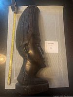 Full side view of the African statue showing the entire figure from head to base with measuring scale beside for size reference.
