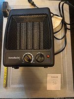 Front-angle photo of a black HomeBasix heater showing two control knobs, metal grille, power cord, and red indicator light.