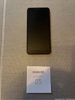 Front view of LG K20 cell phone showing the touchscreen display, placed on a textured surface with a MaxSold label beneath it.