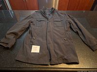 Full frontal view of men's RW&Co jacket in dark color laid flat showing front flap pockets with buttons and zipper closure.