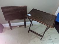 One foldable teak wood table standing and another folded leaning against the wall