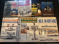 Photo showing nine war-related books laid out on a surface, including titles about Scotland's war, aircraft, World War II, bridge Hitler, the duel, civil aircraft, fighters, and sea warfare.