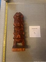 Front view of the wooden monkey statue showing detailed facial features and textured carving with a measuring tape indicating size around 9 inches.