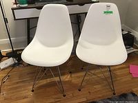 Front view of two white plastic chairs with metal Eiffel legs side by side on wood floor in front of a desk.