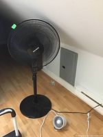 Pelonis black stand fan and small black table fan on a hardwood floor, showing their relative sizes and designs.