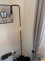 Full view of the floor lamp showing the tall black metal stem, curved arm, exposed bulb, and flat round base.