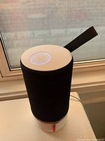 Full view of the Libratone ZIPP 2 speaker showing black fabric body, white base, and hanging strap on windowsill.