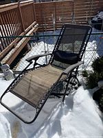 Side angle showing the full reclined folding lounger on snow-covered ground.